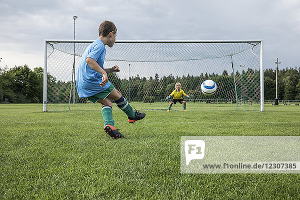 Junger Fußballspieler kickt Ball vor dem Tor mit Torhüter