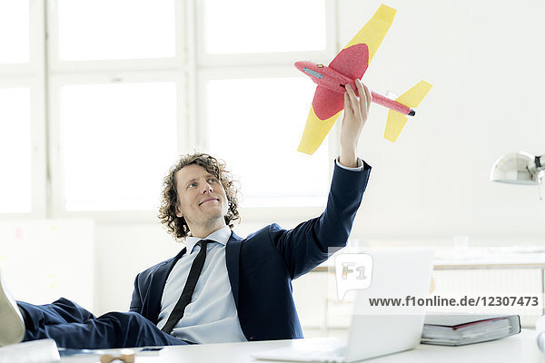 Geschäftsmann sitzt in seinem Büro und spielt mit einem Spielzeugflugzeug.