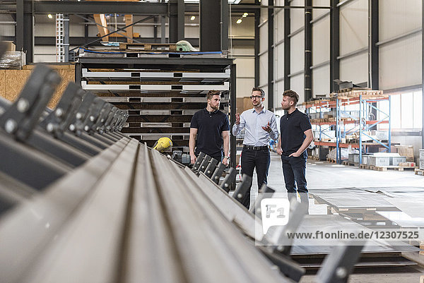 Three men talking on factory shop floor