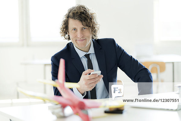 Geschäftsmann mit Smartphone  Spielzeugflugzeug auf seinem Schreibtisch