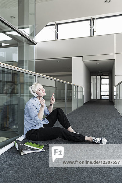 Woman sitting on office floor enjoying listening to music with headphones