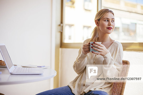 Blonde woman with cup of coffee looking out of the window