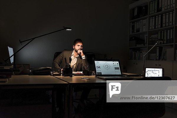 Nachdenklicher Geschäftsmann sitzt nachts am Schreibtisch im Büro.
