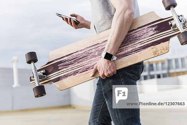Nahaufnahme des Mannes mit Handy und Skateboard im Parkhaus