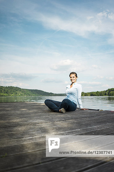 Lächelnde Frau sitzt auf einem Steg am See