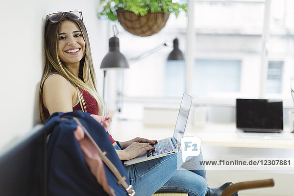 Smiling casual young woman using laptop in the office