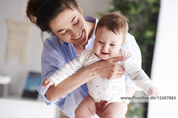 Glückliche Mutter trägt ihr Baby zu Hause.