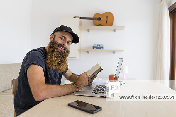 Portrait of bearded young man sitting at desk with laptop and notebook