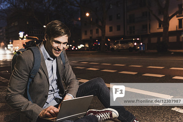 Lächelnder Geschäftsmann mit Laptop in der Stadt bei Nacht