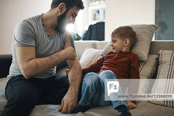 Father sitting on the couch with little son showing his tattoo