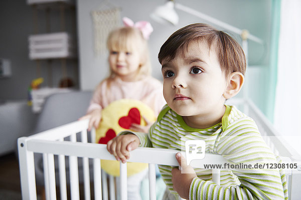 Portrait of toddler in crib with his sister in the background