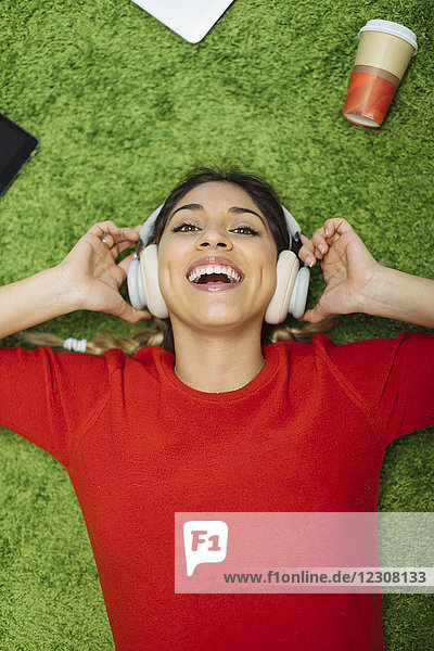Fröhliche junge Frau liegt auf dem Teppich und hört Musik mit Kopfhörern.