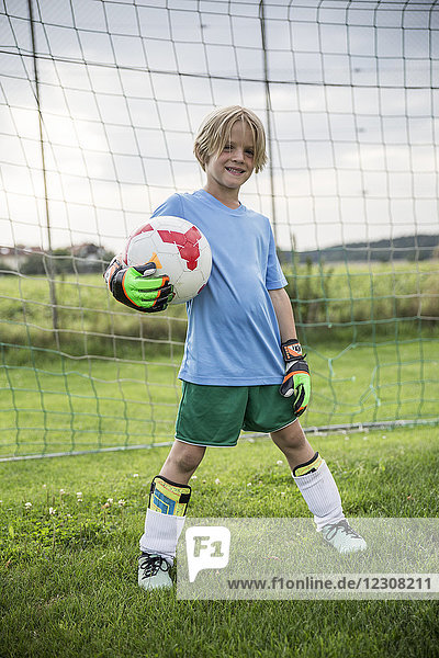 Porträt eines lächelnden jungen Fußballtorhüters  der den Ball auf dem Fußballplatz hält.