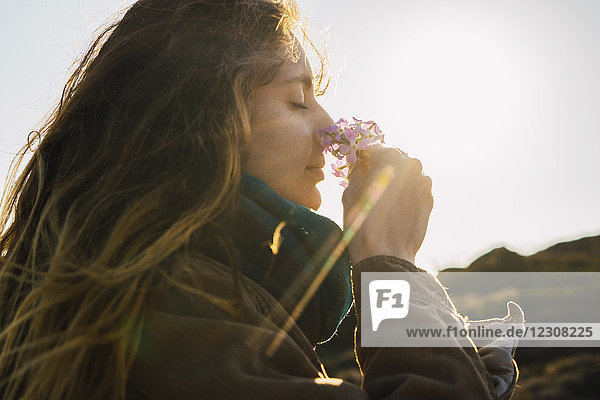 Frau im Sonnenlicht genießt den Duft einer Blume