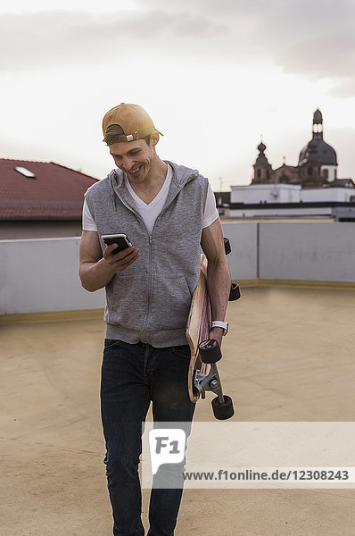 Lächelnder Mann mit Handy und Skateboard im Parkhaus