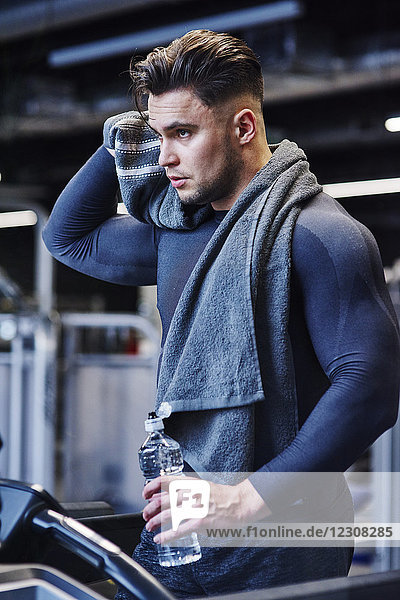 Mann mit Wasserflasche auf dem Laufband im Fitnessstudio