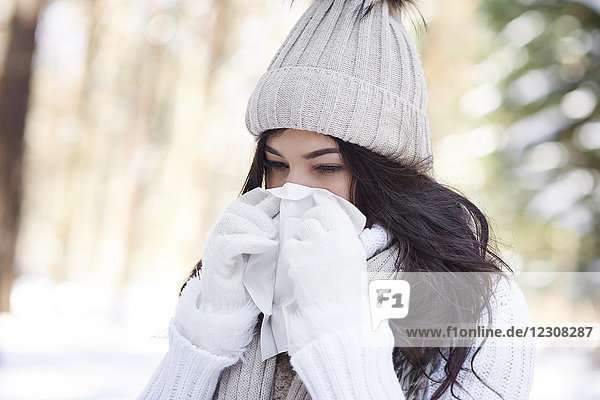 Junge Frau beim Nasenblasen im Winter
