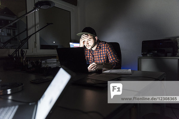 Porträt eines Freiberuflers  der nachts am Schreibtisch sitzt und am Laptop arbeitet.