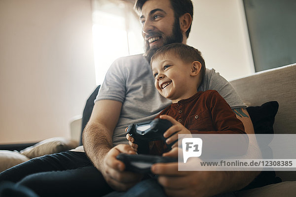 Happy father and little son sitting together on the couch playing computer game