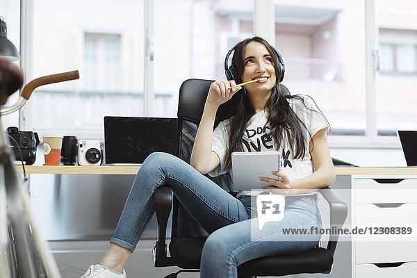 Lässige junge Frau mit Notizblock und Kopfhörer im Coworking Space