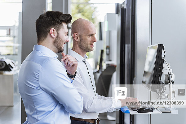 Zwei Geschäftsleute in der Firma  die sich am Computer unterhalten.
