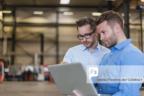 Two businessmen sharing laptop on factory shop floor