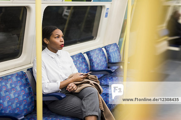 UK  London  businesswoman with cell phone sitting in underground train