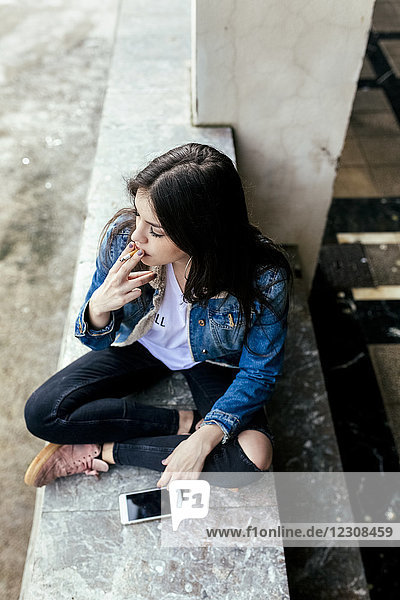 Young woman sitting on a wall smoking a cigarette