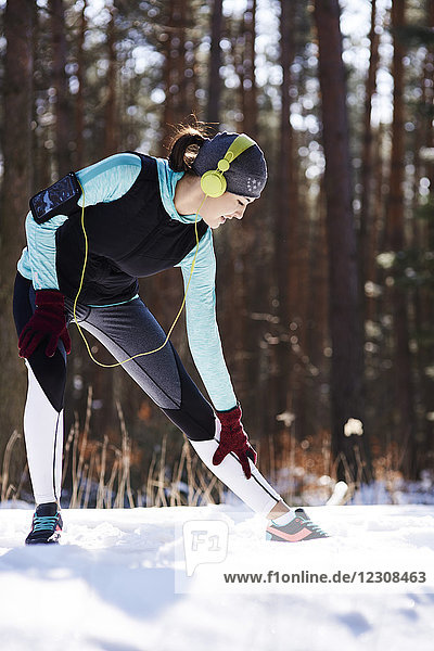 Young woman with headphones doing tretching exercise in winter forest