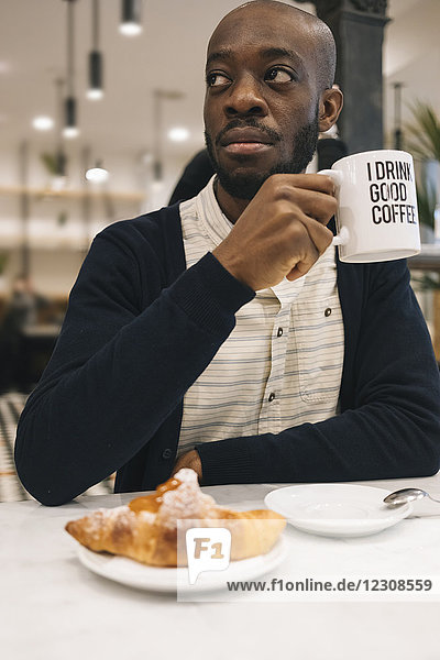 Man with croissant and cup of coffee in a cafe looking around
