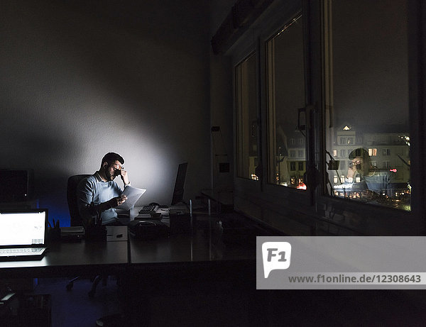 Exhausted businessman sitting at desk in his office by night