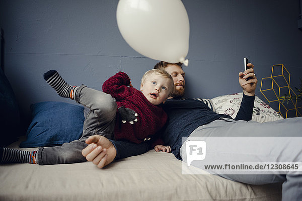 Vater liest SMS  während der Sohn mit einem Ballon spielt.