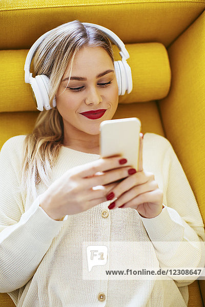 Blonde Frau mit Kopfhörer über Smartphone zu Hause