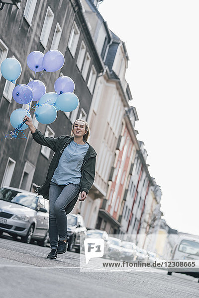 Glückliche Frau mit blauen Luftballons auf der Straße