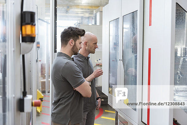 Two men examining machine in modern factory