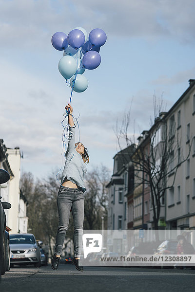 Junge Frau mit blauen Luftballons  die auf der Straße in die Luft springen.