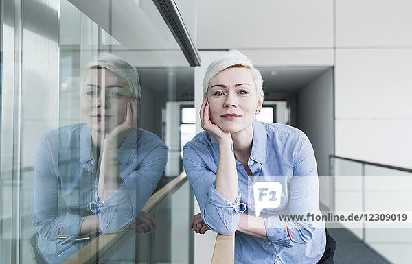Porträt einer Frau auf Büroetage  die sich auf das Geländer stützt