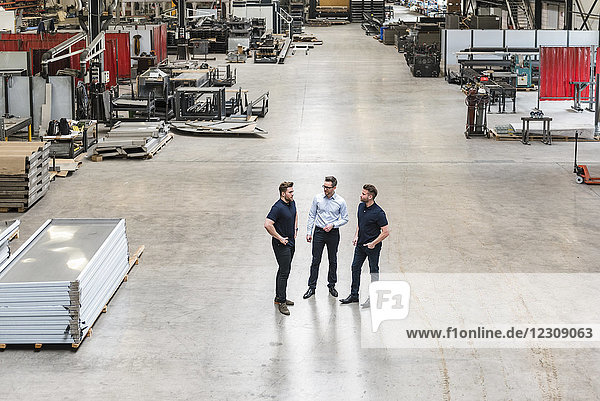 Three men standing and talking on factory shop floor