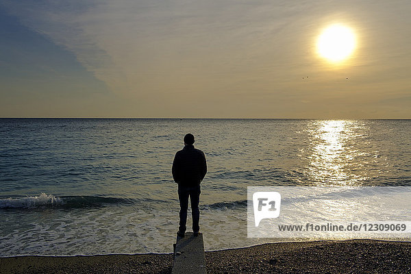 Italy  Liguria  Riviera di Ponente  Noli  man standing at beach at sunrise