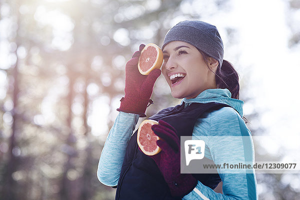 Porträt einer lachenden jungen Frau in Sportbekleidung mit zwei Hälften Grapefruit