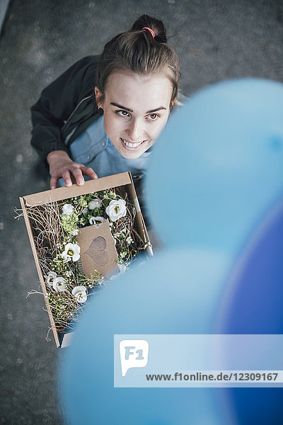 Porträt der lächelnden Frau mit Geschenk im Karton und blauen Luftballons nach oben schauend