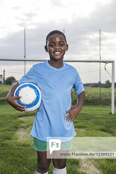 Porträt eines lächelnden jungen Fußballspielers  der den Ball auf dem Fußballplatz hält.