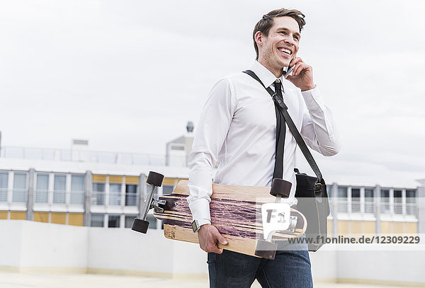 Glücklicher Geschäftsmann mit Handy und Skateboard im Parkhaus