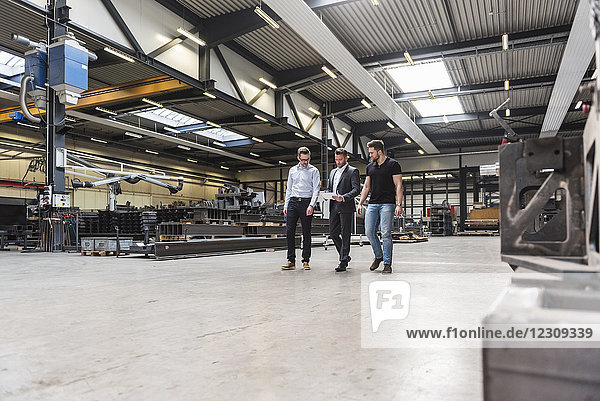 Three men with tablet walking and talking on factory shop floor
