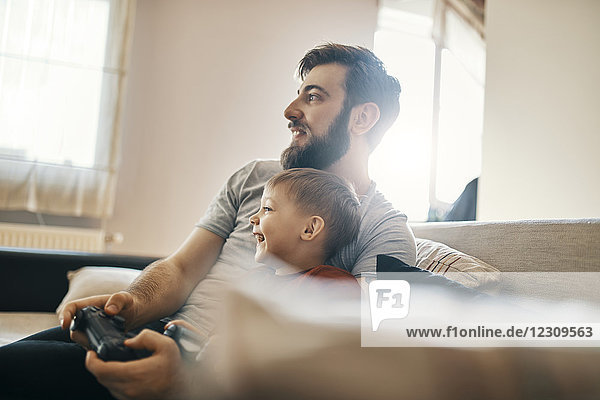 Father and son sitting together on the couch playing computer game