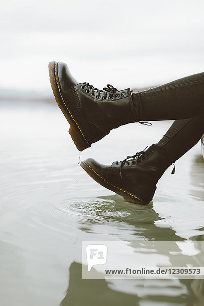 Frau in schwarzen Stiefeln  die die Wasseroberfläche des Sees berühren  Teilansicht
