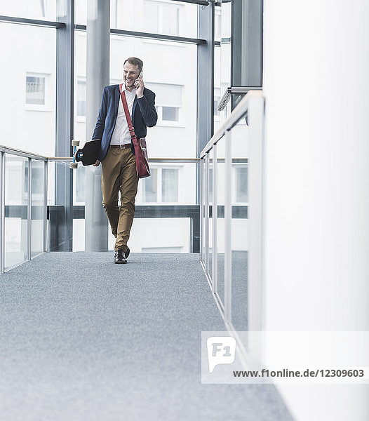 Smiling businessman holding skateboard and talking on cell phone