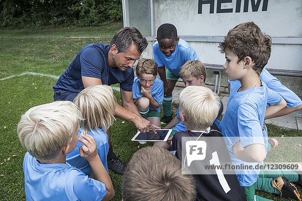 Trainer mit Tablette und jungen Fußballspielern auf dem Fußballplatz
