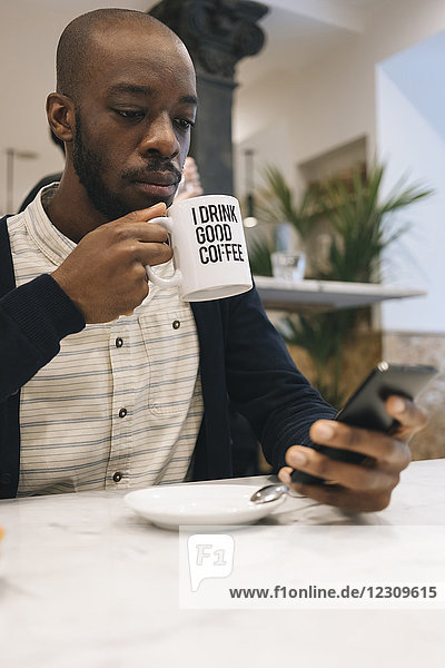 Mann mit Tasse Kaffee in einem Café mit Handy