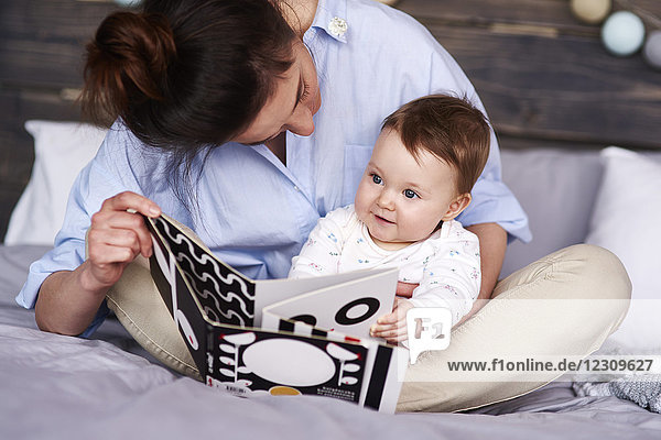 Mother and baby watching a picture book on bed at home